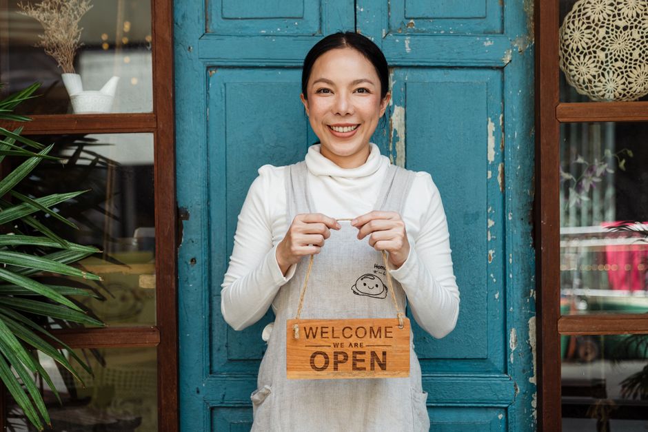 Ladeninhaberin mit „Welcome – we are open“-Schild vor ihrem Geschäft